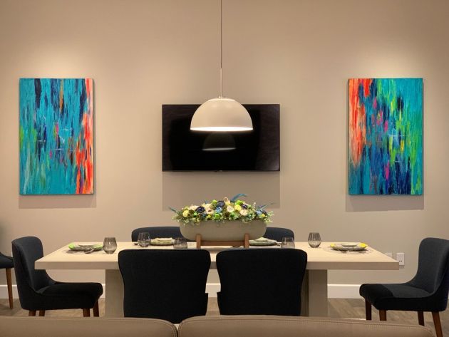 Another view of a showroom gallery wall featuring an array of modern paintings in various sizes, set against a neutral backdrop with soft, ambient lighting.