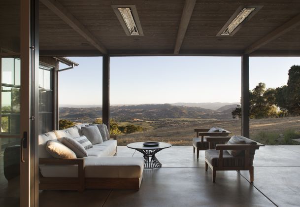 A modern covered outdoor patio with comfortable seating and a panoramic view of rolling hills and countryside.